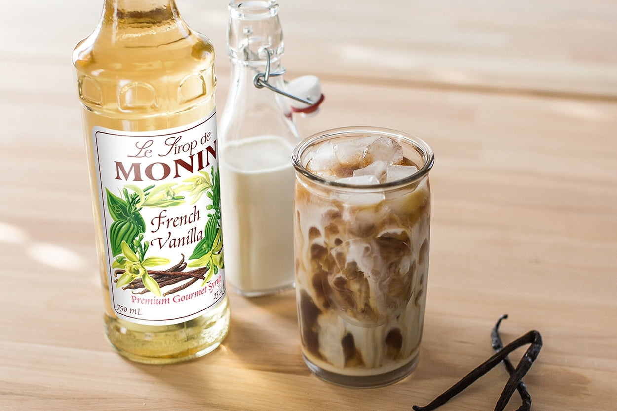 bottle of Monin 750ml french vanilla and an iced drink glass mixed with milk and Monin syrup on the table