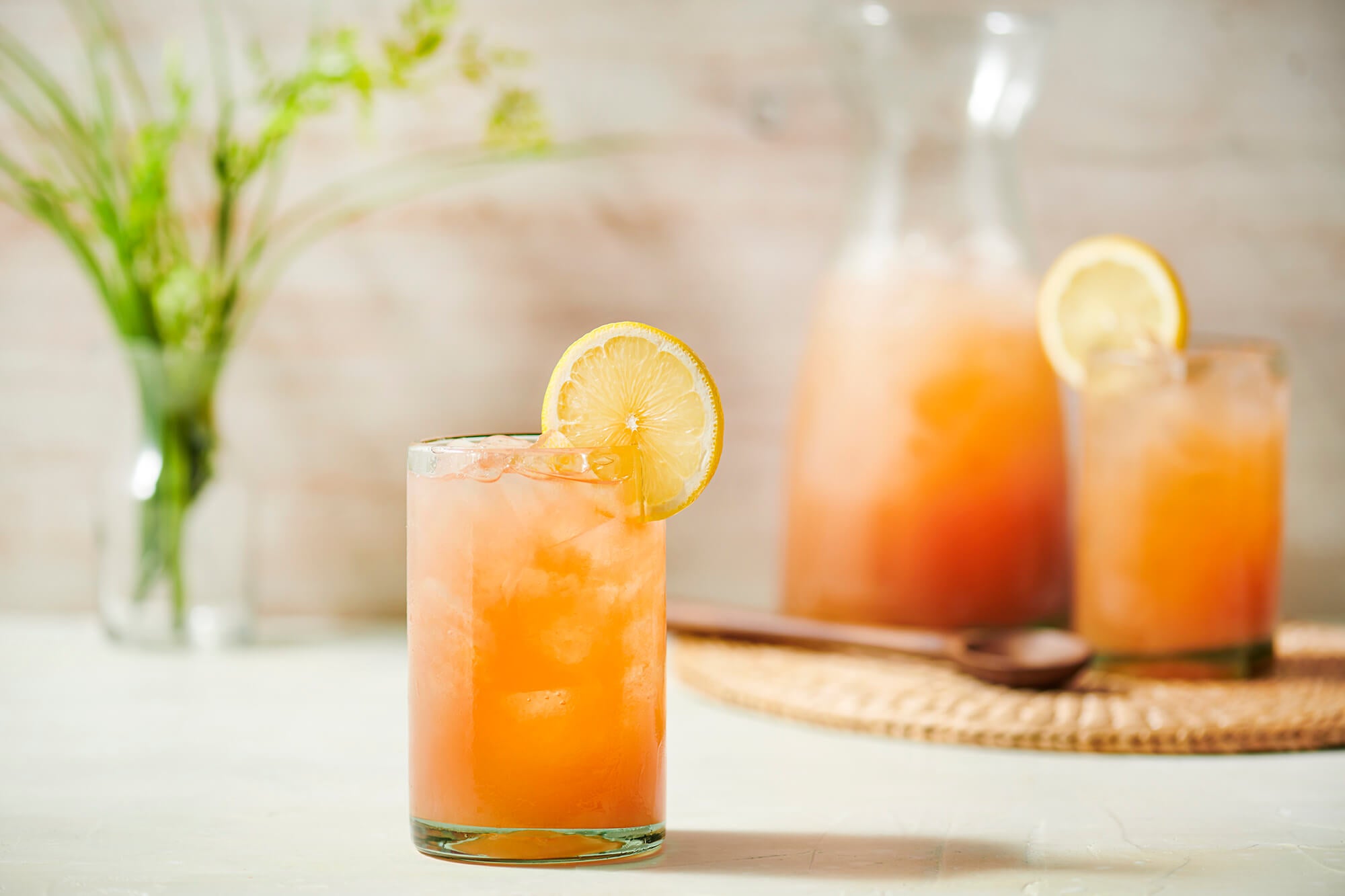 a glass of iced tea in the forefront, a pitcher of tea and another glass in the background