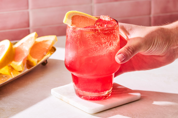 Iced ruby red grapefruit mocktail with a grapefruit slice garnish on a marble coaster.