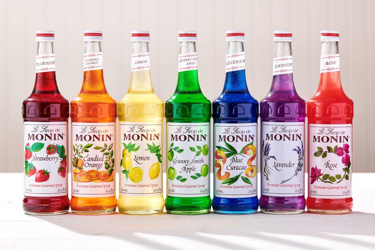 Seven glass Monin bottles lined up in rainbow order