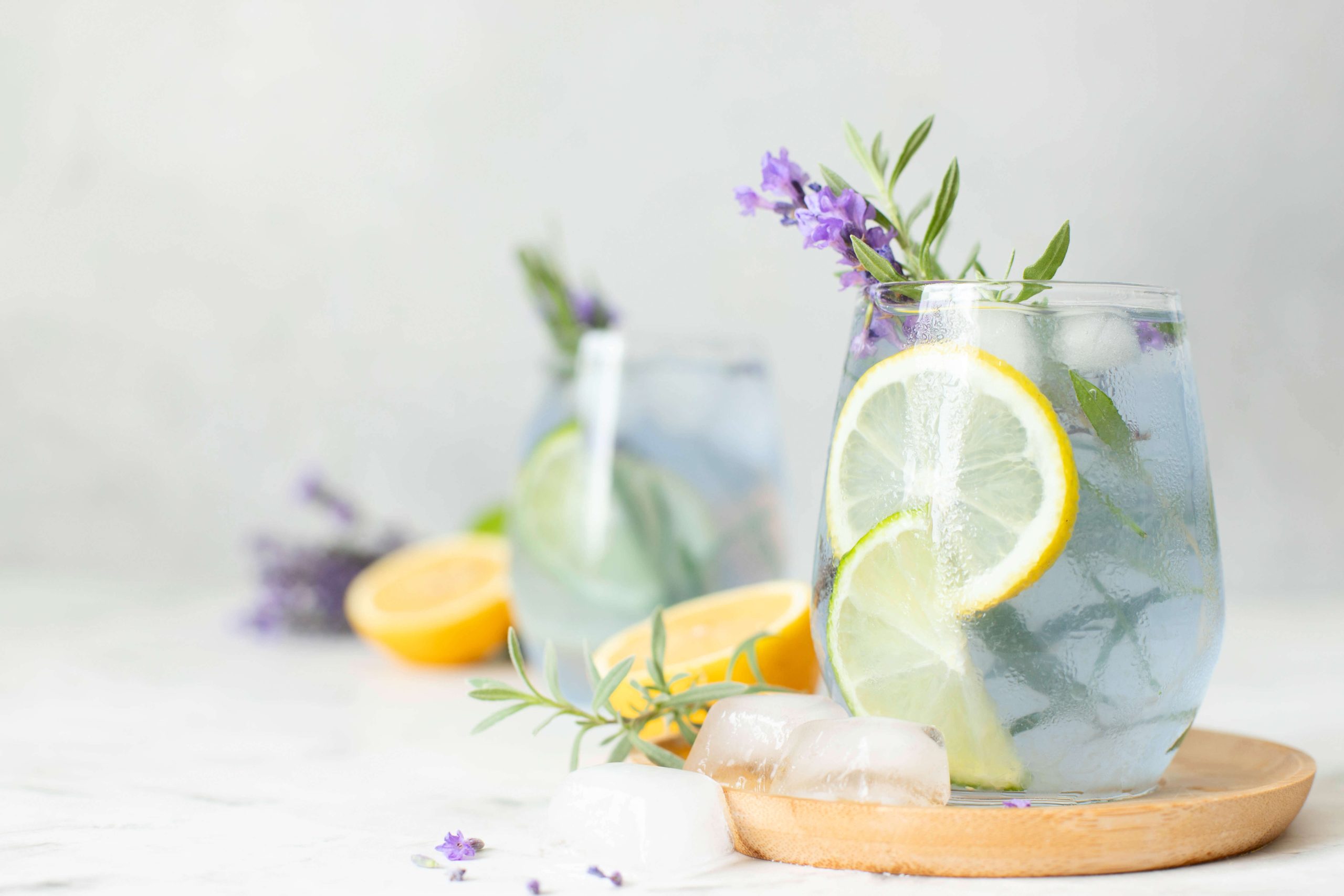 A stemless wine glass filled with a light colored spritz, garnished with lemon wheels and purple flowers.