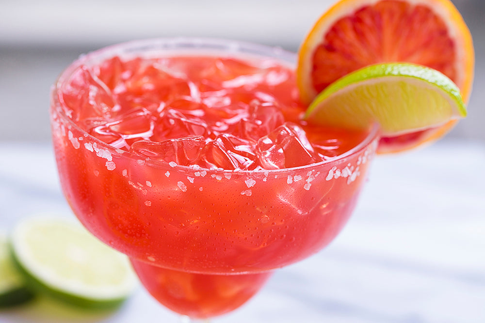 Close up of blood orange margarita with a salt rim and a blood orange and a lime wedge.