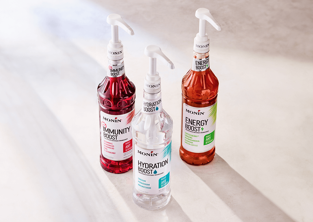 A bottle of Monin Total Immunity Boost, Monin Hydration Boost, and Monin Energy Boost against a neutral background