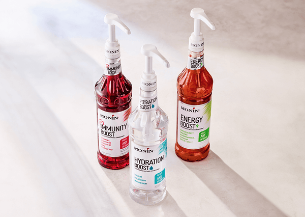 A bottle of Monin Total Immunity Boost, Monin Hydration Boost, and Monin Energy Boost against a neutral background