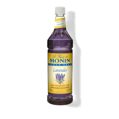 A bottle of Monin Lavender sugar-free syrup on a white background with a soft shadow. The bottle is filled with deep purple liquid and features a yellow and blue label with lavender illustrations.