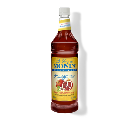 A bottle of Monin sugar-free pomegranate syrup on a white background with a soft shadow. The bottle is filled with deep red syrup and features a yellow label with blue and red text, along with an illustration of a pomegranate.