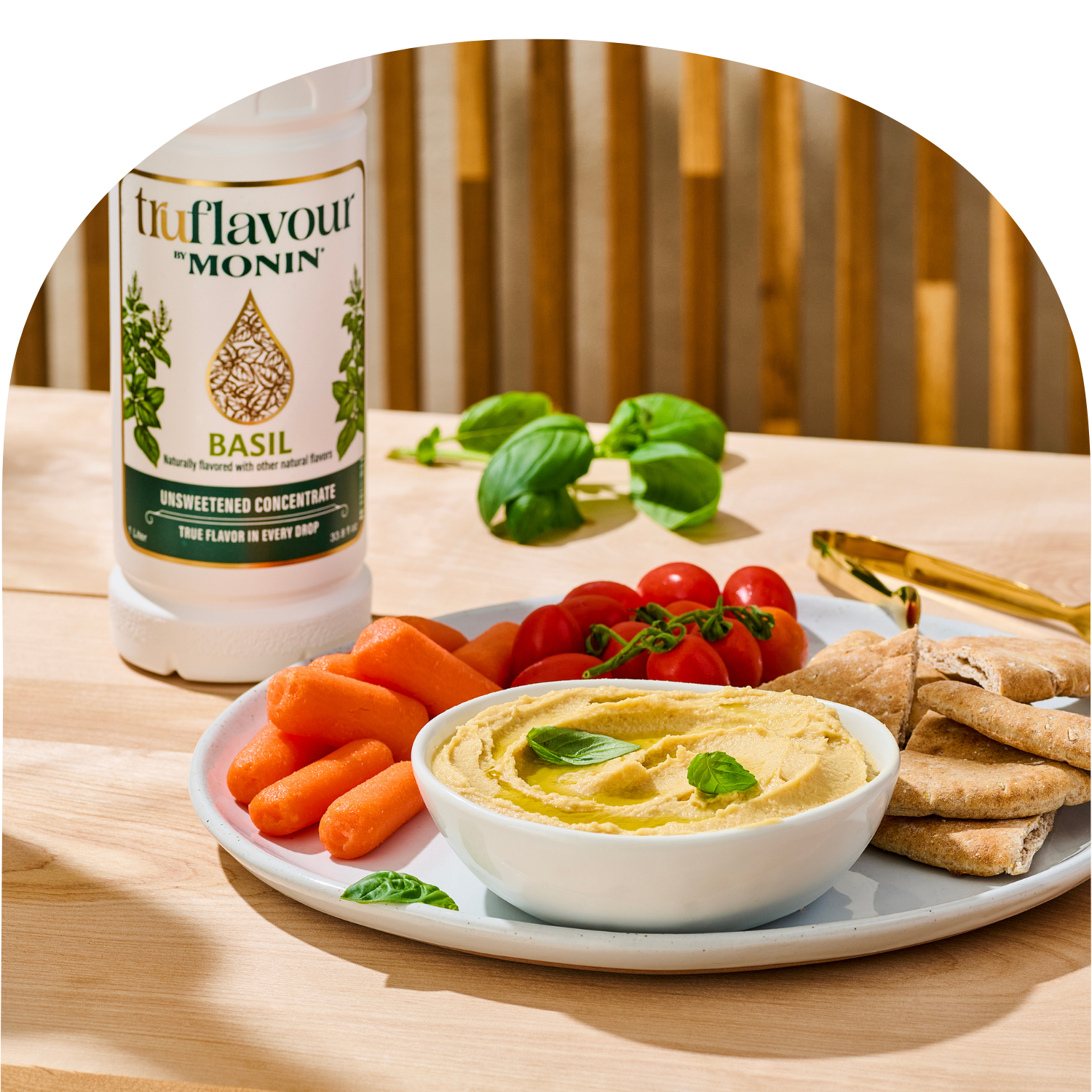 Bottle of Monin basil flavor concentrate next to a plate with hummus, vegetables, and pita bread.