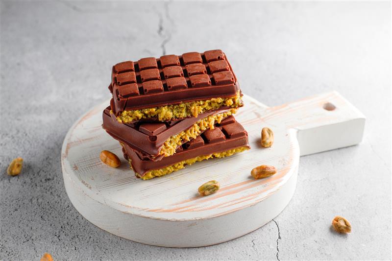 Dubai chocolate bar cut in half, revealing creamy green pistachio filling and crunchy kataifi bits. it sit on a marble tray