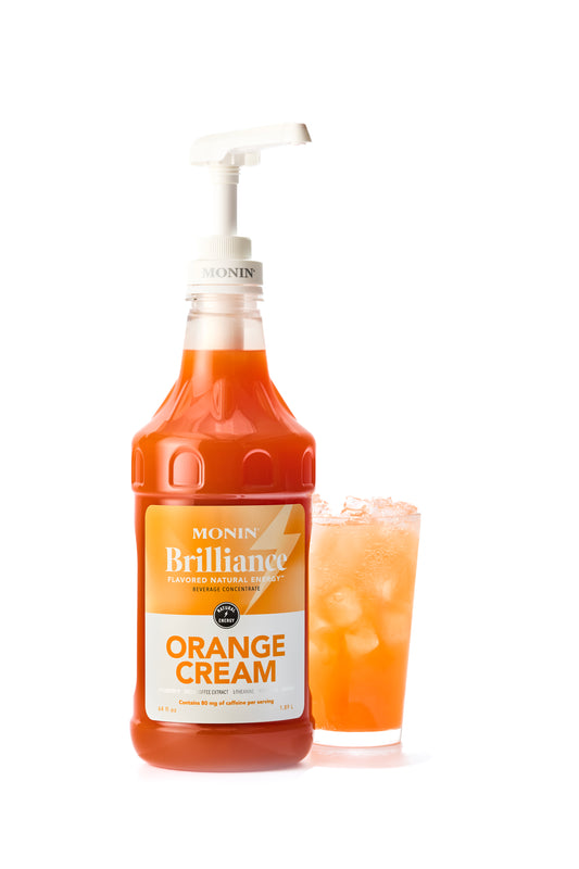 Monin Brilliance Orange Cream syrup bottle with a pump and a glass of orange cream shake on a white background