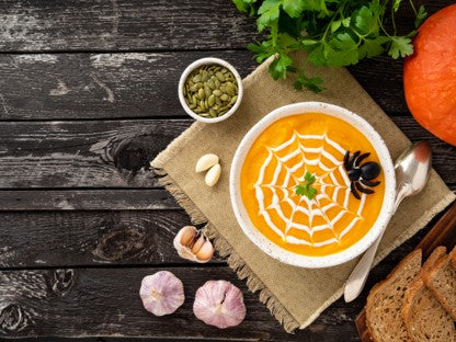 Spooky Halloween-themed soup with spider web design on a wooden table.