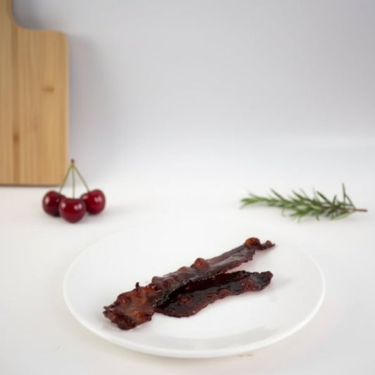Candied bacon glazed with Monin Black Cherry Fruit Purée served on a white plate
