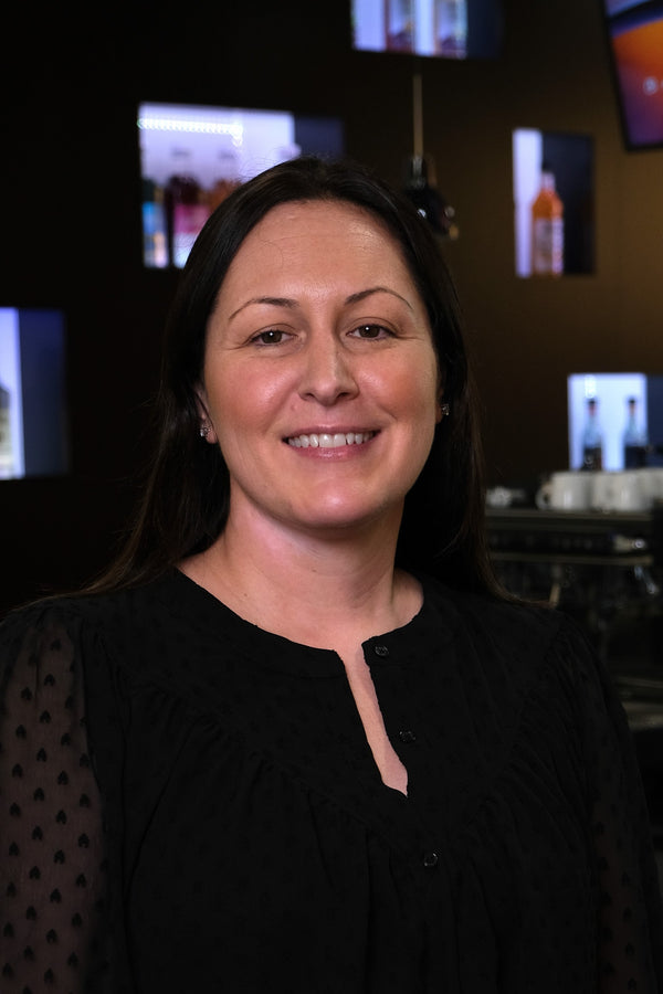 Woman standing in a bar setting with drinks and televisions in the background