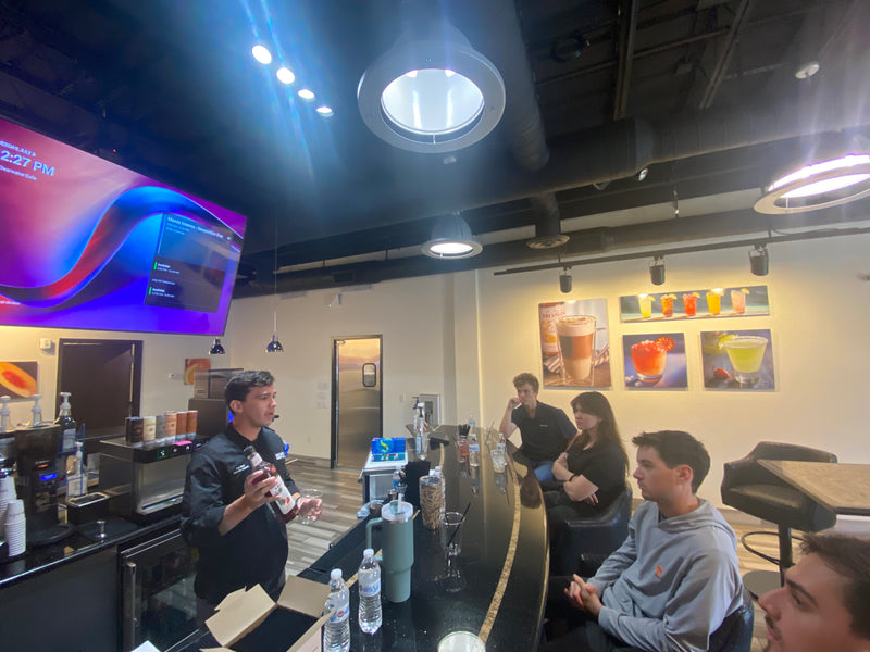 People sitting at a bar with a large screen displaying colorful graphics in a casual setting.