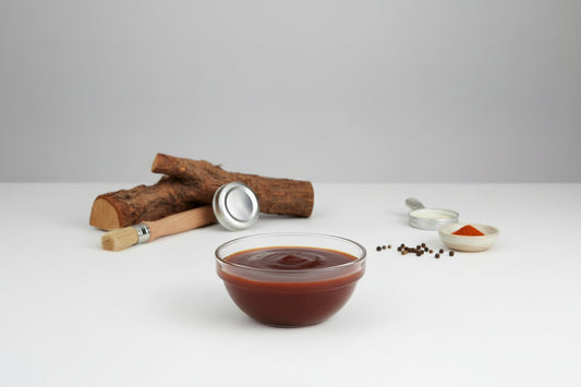 Bowl of dark brown sauce with wooden logs and measuring spoons on a white surface