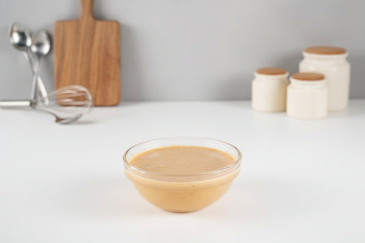 Glass bowl of creamy beige sauce on a white background with a few kitchen elements