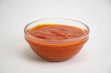 Clear glass bowl filled with red sauce on a white background