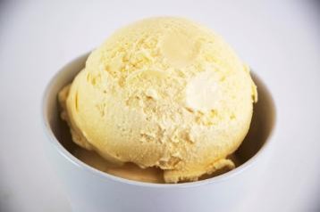 Yellow ice cream in a white bowl on a light gray background