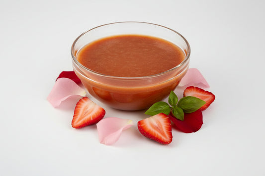 Red sauce in a glass bowl with a few roses and strawberries on the side. 