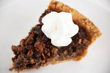 A slice of pecan pie topped with a swirl of whipped cream on a white plate.