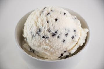 A scoop of peppermint chip ice cream with chocolate chips served in a white bowl.
