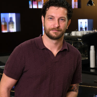 Man standing in a bar setting with drinks and equipment in the background