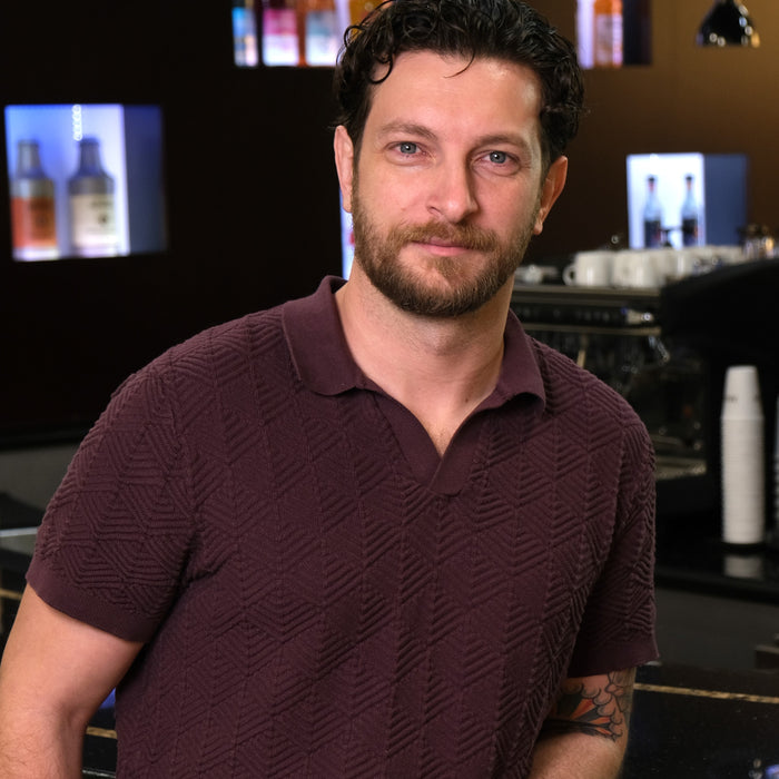 Man standing in a bar setting with drinks and equipment in the background